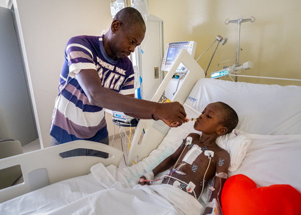 Woodmylens’ father, Jean, feeds him juice after surgery.